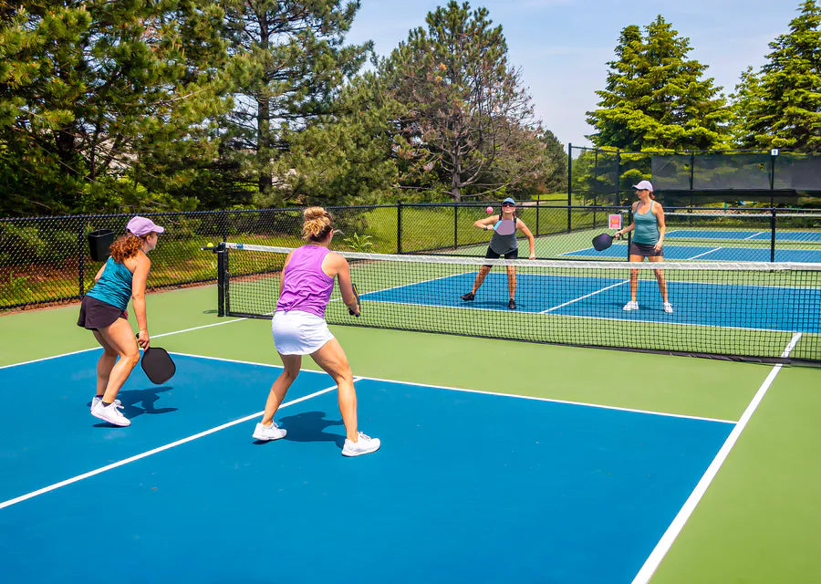 Four people playing doubles pickleball on outdoor blue courts, illustration for the history and origin of pickleball name