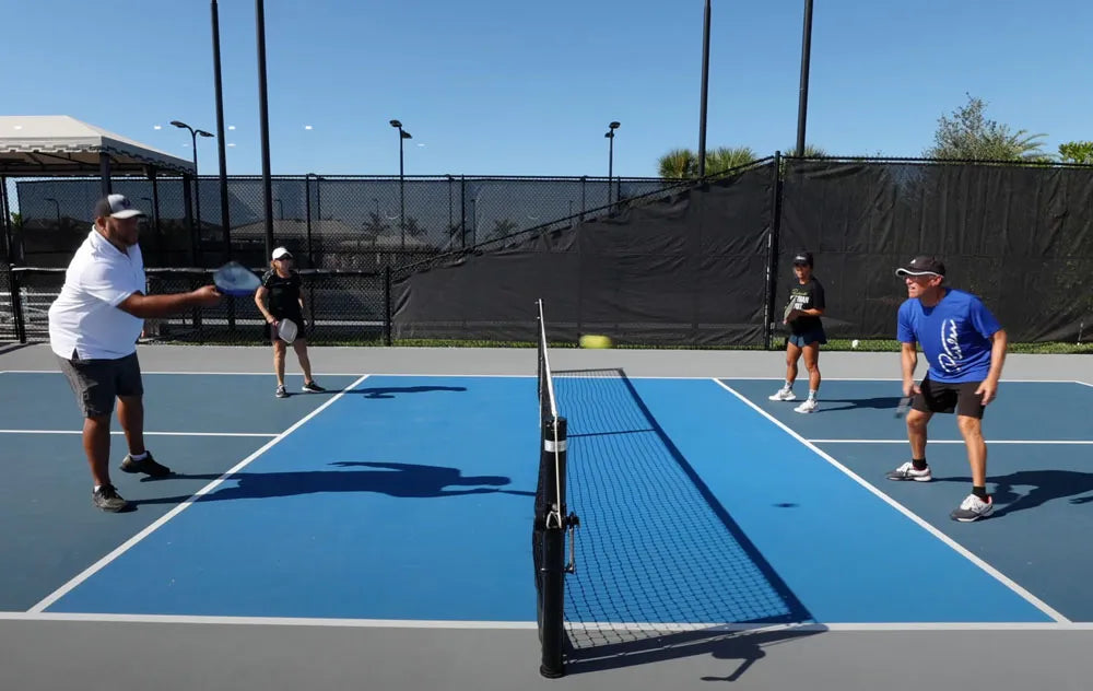 Four pickleball players positioned at the kitchen non-volley zone line during a doubles match rally
