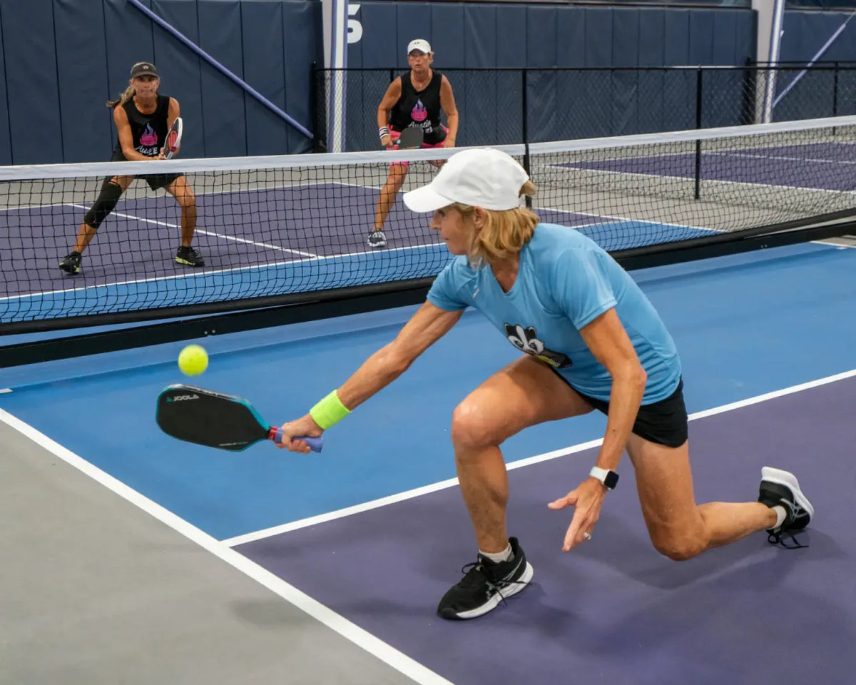 A pickleball player crouching near the kitchen line to hit a low, controlled dink shot over the net